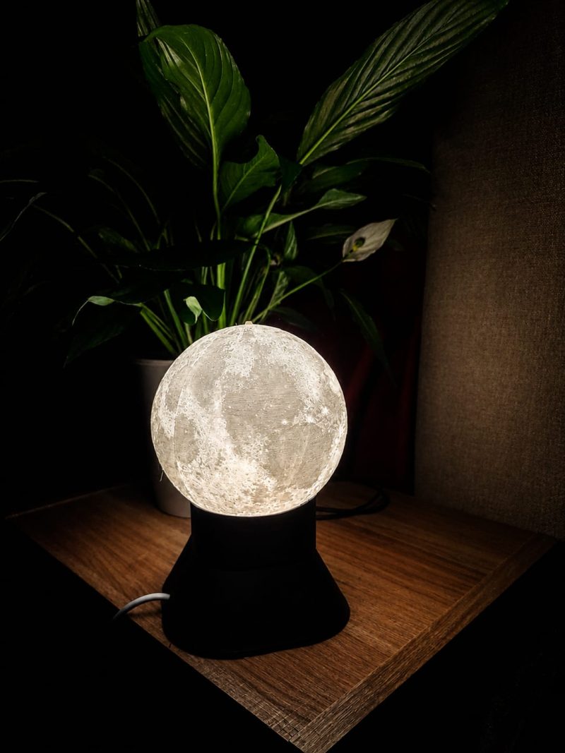 Textured 3D-printed moon lamp glowing on a wooden table next to a peace lily in Muizenberg.